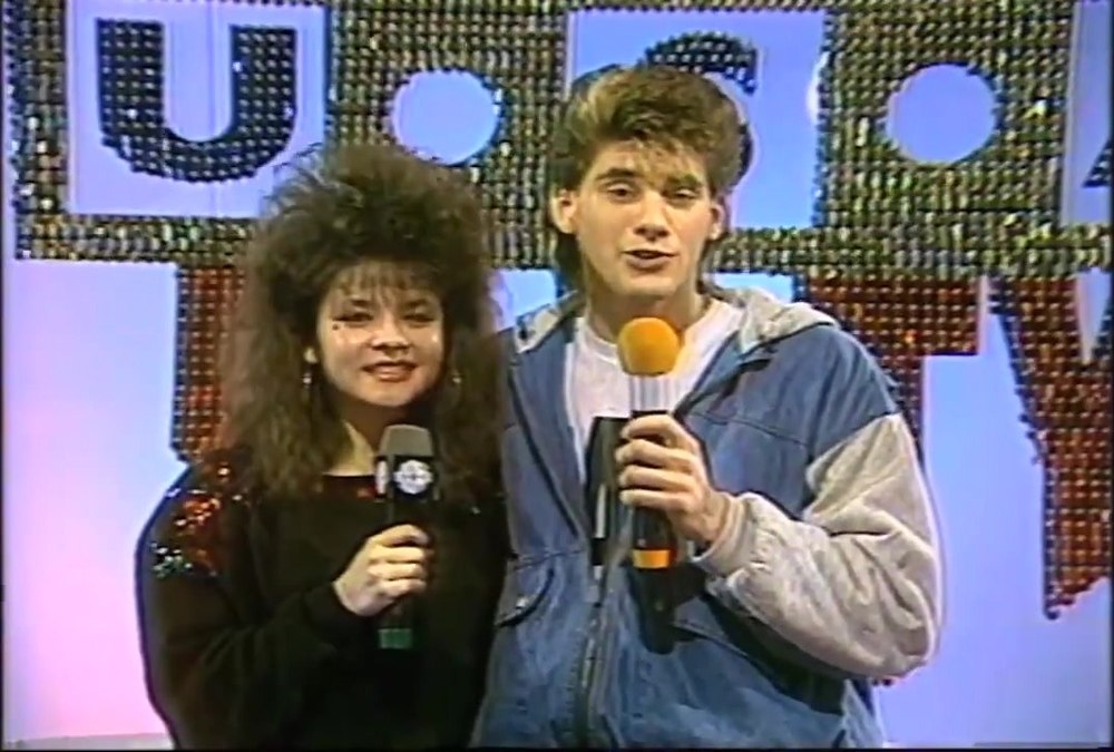 Two Dance Party USA cast members on camera in front of the studio sign